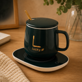 Green ceramic mug with lid, gold spoon, and electric mug warmer on a wooden desk.
